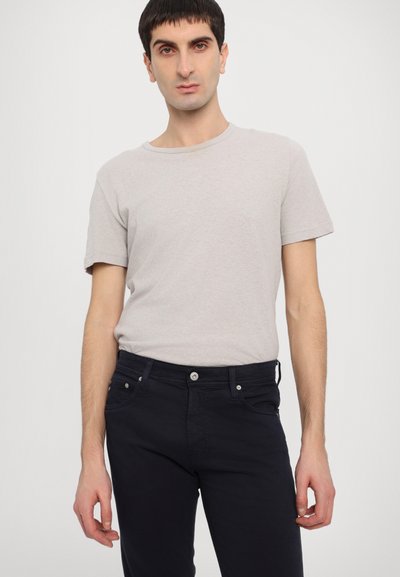 Ανοιχτό γκρι βαμβακερό T-shirt με στρογγυλή λαιμόκοψη, σε συνδυασμό με σκούρες μπλε τζιν παντελόνια που διαθέτουν κλείσιμο με κουμπί και μπροστινές τσέπες.