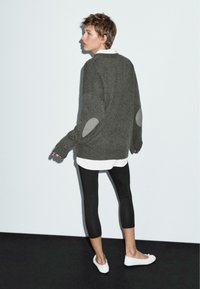 Grå oversized tröja med armbågspatchar, vit skjorta under, svarta leggings och vita skor; texturerat stickat material.