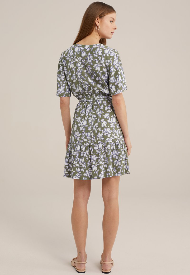 Rochie florală verde cu mâneci scurte, tiv cu volane în straturi și talie ajustată. Prezintă un model cu flori albe și purpurii. Sandale plate.