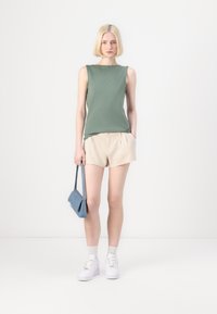 Grønn, ermeles topp, beige shorts, blå håndveske, hvite joggesko, brukt med ankelsokker. Enkelt, uformelt og moderne design.
