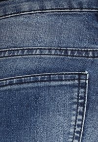 Los jeans de mezclilla presentan un color azul oscuro con costuras visibles. La tela tiene una textura suave, exhibiendo un bolsillo trasero y un sutil desvanecimiento.