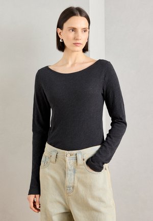 Haut noir à manches longues avec un large encolure, associé à un jean bleu clair taille haute, présentant une coupe décontractée et relax. 