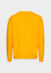 Sudadera amarilla con cuello redondo, mangas largas y puños acanalados. Textura suave, diseño simple y sin logotipos ni patrones visibles.