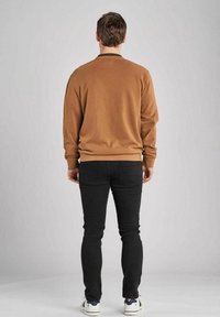 Brun sweatshirt med rund hals, mjuk textur, ribbad nederkant. Kombinerad med slim-fit svarta jeans och vita sneakers. Bakifrån.