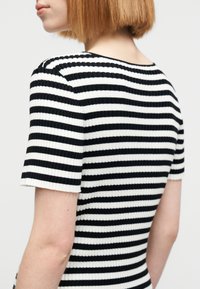 Μαύρο και άσπρο ριγέ τοπ με ραβδώσεις και κοντά μανίκια, με εφαρμοστή σχεδίαση και απαλή υφή, που φαίνεται από πίσω.