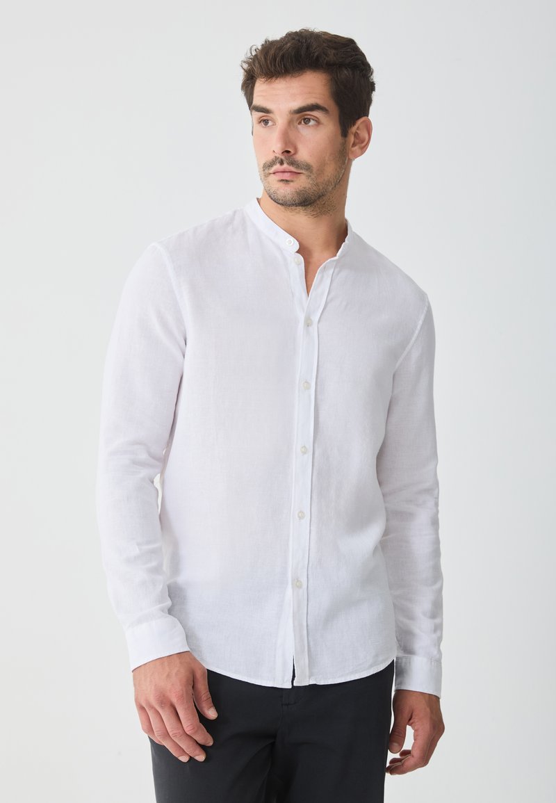 Witte linnen shirt met een bandkraag en lange mouwen, met een knoopsluiting aan de voorkant en een rechte zoom, gedragen met donkere broeken.