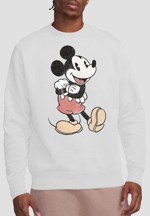 Person wearing white sweatshirt featuring classic Mickey Mouse cartoon character with red shorts and large yellow shoes.