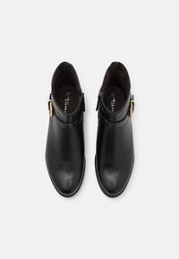 Botas de tobillo de cuero negro con punta redonda, cremallera lateral y un acento de hebilla dorada. Textura suave y diseño minimalista. Talla 37.