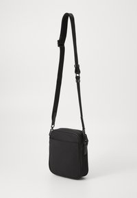 Black crossbody bag made of durable fabric, featuring a rectangular shape, adjustable strap, and a zippered top. Front pocket included.