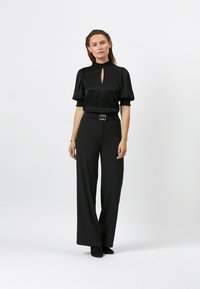 Zwarte blouse met sleutelgatdetail en korte pofmouwen, gecombineerd met zwarte wijde pantalons en een bijpassende riem. Gladde stofstructuur.