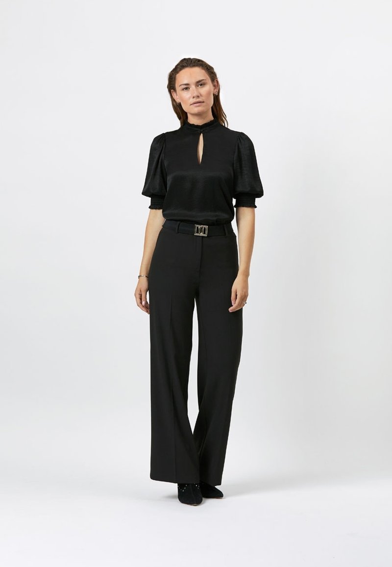 Zwarte blouse met sleutelgatdetail en korte pofmouwen, gecombineerd met zwarte wijde pantalons en een bijpassende riem. Gladde stofstructuur.