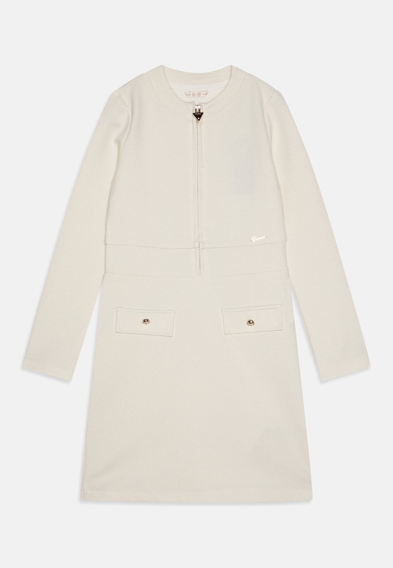Kremfarget langermet kjole med teksturert stoff, frontglidelås, to brystlommer med trykknapper, og en liten logo ved kanten.