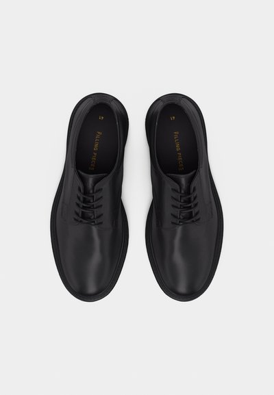 Ζευγάρι μαύρα δερμάτινα παπούτσια δετά με στρογγυλεμένες μύτες, σε στάση από πάνω, πάνω σε λευκό φόντο.