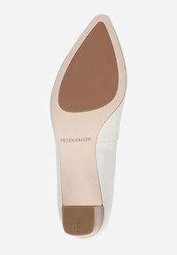 Chaussure en cuir blanc avec un bout pointu, une tige lisse et une semelle en caoutchouc marron clair comportant un texte imprimé sur le talon.
