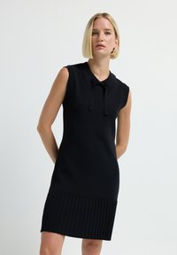 Abito nero senza maniche con colletto e dettaglio cravatta a fiocco, caratterizzato da una texture plissettata all'orlo. Realizzato in un tessuto liscio ed elastico.