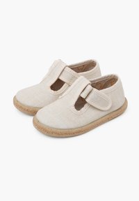 Beige canvas schoenen met een klittenbandsluiting, afgeronde tenen en een jute zool. Beschikt over uitsnijdingen aan de zijkanten en een lichte textuur.
