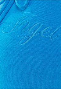 Turquoise fabric with a soft texture features an embroidered "Angel" in a contrasting blue hue. The design is sleek with no additional patterns.