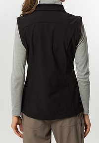 Gilet nero senza maniche con colletto, realizzato in tessuto liscio, caratterizzato da una vestibilità sartoriale e sottili cuciture laterali. Indossato sopra una maglia grigia a maniche lunghe.