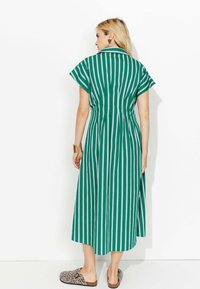 Robe midi rayée verte et blanche avec des manches courtes, un col et une taille élastique. Portée avec des mules à imprimé léopard.