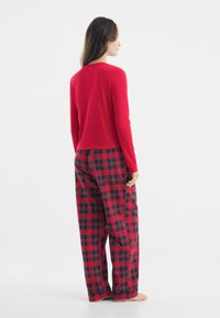 Red long-sleeve top with textured surface paired with checkered red and black plaid pajama pants. Casual, loose fit.
