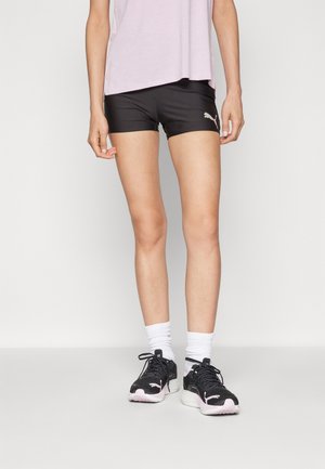Shorts de sport noirs avec une coupe ajustée et un logo doré sur le côté, associés à des baskets noires avec des accents roses et des chaussettes blanches à la cheville.