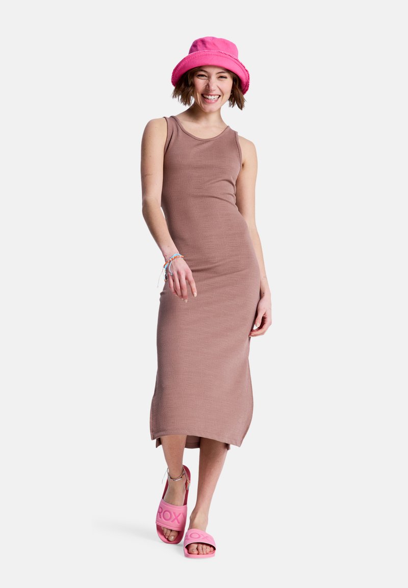 Braunes, geripptes Tankkleid, knielang mit seitlichem Schlitz. Dazu leuchtend pinke Pantoletten mit erhabenen Buchstaben und ein pinker Bucket-Hut.