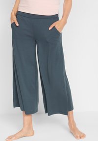 Pantaloni a gamba larga realizzati in morbido tessuto color teal scuro, con una cintura elastica e tasche laterali, dalla texture liscia e design alla caviglia.