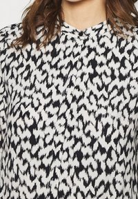 Svart och vit blus med ett distinkt djurtrycksmönster, lättviktsmaterial och krage med knappar.