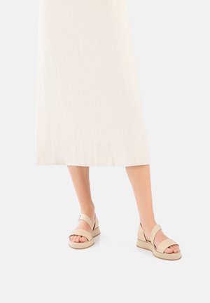 Beige wedge sandals featuring two wide straps across the foot with a smooth finish and a textured sole. Accented with a small buckle.