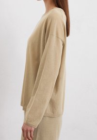 Licht beige lange mouw sweatshirt in een zachte, gestructureerde stof. Het heeft een ronde halslijn en een ontspannen pasvorm, met verlaagde schoudernaden.