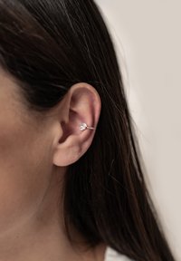 Silberner Ohrclip mit zwei kleinen klaren Edelsteinen, geschwungenes Design, das auf dem oberen Ohr sitzt, und dabei glattes Metall und zarte Details präsentiert.