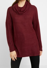 Top a maniche lunghe color vino con collo a scialle, realizzato in tessuto morbido. Presenta una vestibilità rilassata e spacchi laterali vicino all'orlo.