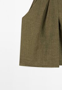 Oliwkowo-zielony, teksturowany materiał o luźnym kroju i plisowanym wzorze. Posiada głębokie kieszenie boczne oraz prosto wykończony dół, z minimalnymi detalami.