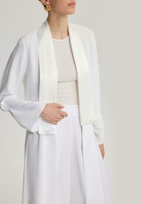 Bela dolga jakna z dolgimi rokavi in odprtim sprednjim delom, svilen material, široki ravni rokavi in gladka tekstura, usklajena z oprijetim belim topom.