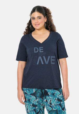 T-shirt V en marine avec le texte imprimé « RIDE THE WAVE ». Tissu doux avec une coupe décontractée, associé à un pantalon à motifs de feuilles vertes.