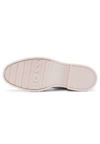 Suela de zapatilla de goma clara, con surcos texturizados paraagarre y el nombre de la marca "BOSS" grabado de manera prominente en el centro.