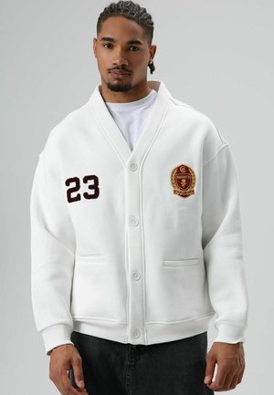 Witte trui met een sjaalkraag, knoopsluiting, twee voorzakken, geborduurd nummer "23" en een logopatch op de borst.