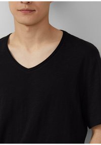 Czarny t-shirt z dekoltem w serek, z krótkimi rękawami, wykonany z lekkiego materiału, o gładkiej strukturze i subtelnej połysku.