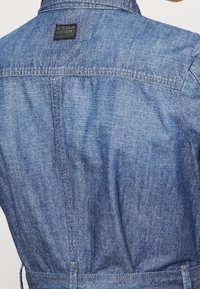 Jeansjacka i ljusblå färg, klassisk krage och synlig sömnad. Inkluderar en märkesetikett på baksidan nära nacken.