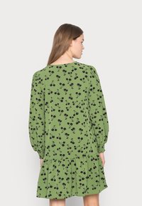 Vestido verde feito de tecido leve com padrão floral preto, mangas bufantes longas, punhos franzidos e design de saia em camadas.