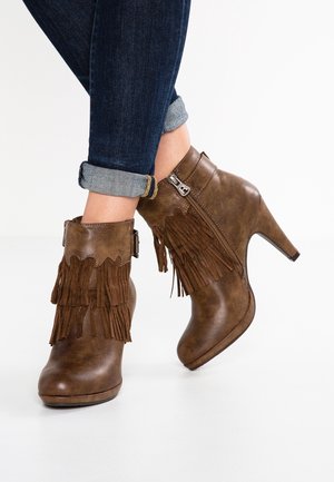 Bottines en cuir marron avec détail à franges et fermeture éclair latérale portées avec un jean bleu foncé retroussé.