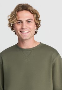 Felpa verde khaki con collo a giro, caratterizzata da un tessuto testurizzato e dettagli di cucitura sottili, adatta per un look casual.