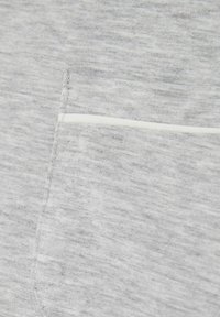 Material de hanorac gri deschis cu un model texturat, melanj, evidențiat de o cusătură albă contrastantă pe marginea unei buzunare.