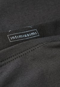 Close-up van zwart stof met een gladde textuur en een zichtbaar etiket met het "intimissimi" logo in het blauw. Stiksel detail langs de rand.