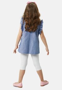 Sininen chambray-tunika, jossa on ryppyiset hihat, yhdistettynä valkoisiin lyhyisiin legginsseihin ja vaaleanpunaisiin ballerinatossuihin. Hiukset ovat vapaina ja niissä on vaaleanpunainen nauha.