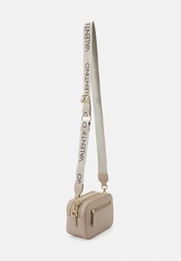 Malá béžová crossbody taška se dvěma zipovými přihrádkami, zlatým kováním a nastavitelným béžovým popruhem potištěným nápisem "VALENTINO" černými písmeny.