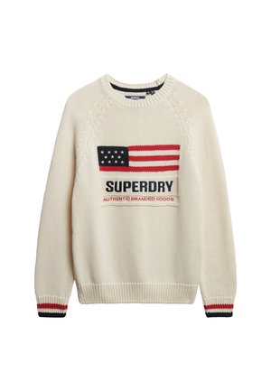Kremowy sweter z dzianiny z wyraźnym wzorem amerykańskiej flagi, z napisem "SUPERDRY" oraz "AUTENTYCZNE TOWARY MARKOWE" w granatowym kolorze. Czerwone i granatowe paski na mankietach.