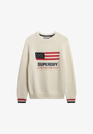 Jersey de punto color crema que presenta un destacado diseño de la bandera americana, con el texto "SUPERDRY" y "AUTHENTIC BRANDED GOODS" en color navy. Puños a rayas en rojo y navy.