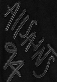 Tessuto nero con lettering in pelle nera in rilievo, realizzato in uno stile corsivo, che mostra il testo "ALISAN 94" su uno sfondo con texture morbida.