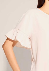 Helles rosa Blusenshirt mit kurzen, Rüschenärmeln. Aus weichem Material gefertigt, mit rundem Halsausschnitt. Glatte Textur, einfaches Design.